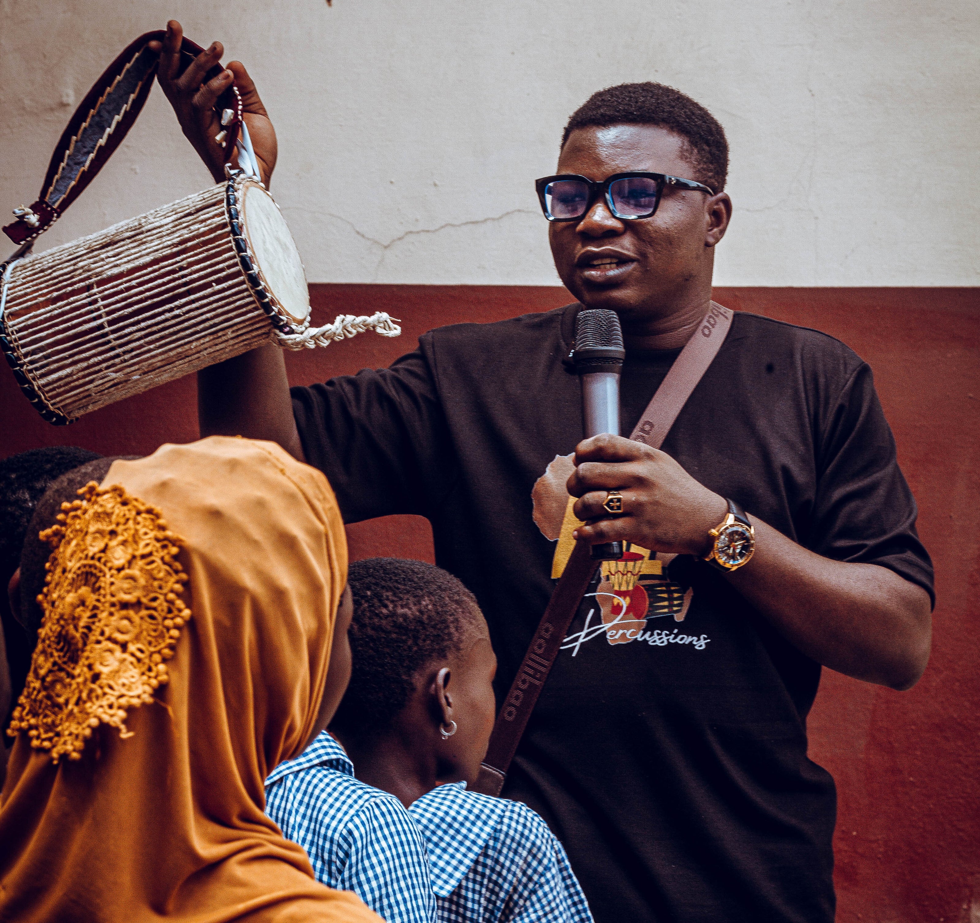 A man holding a drum and a microphone addressing some people